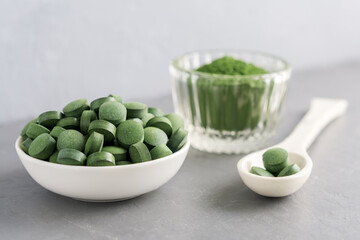 Chlorella or spirulina in the form of tablets and powder on a gray concrete background.