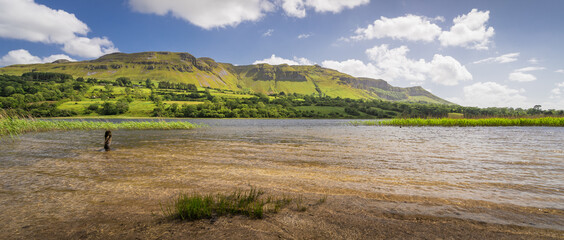 Fototapeta na wymiar Glencar Lough, Leitrim, Ireland. The bright blue skies and summer sun lighting up the hills and the surface of the lake.