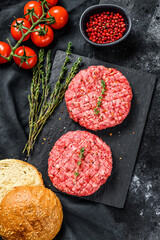 Ingredients for cooking burgers. Minced beef patties, buns, tomatoes, herbs and spices. Black background. Top view