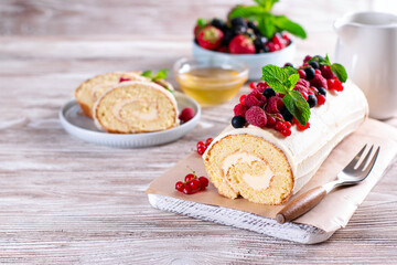 Sponge cake roll filling cream and berries, strawberry, raspberries, blueberry and red currants on white wooden background