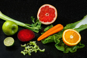Vegetables and fruits healthy food dropping out on dark background. Fresh orange, apple, lime, carrot, salad, beet and celery.