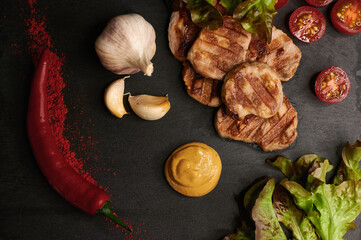 on a dark background medallions of pork with vegetables close-up from above