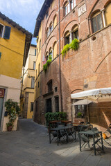 Fototapeta na wymiar Lucca, Italy - August 14, 2019: Old narrow medieval street with cafe and shops in the historic center of Lucca, Tuscany, Italy
