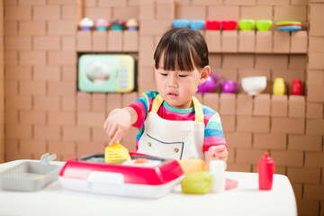 Obraz na płótnie Canvas toddler girl pretend play food preparing role against cardboard blocks kitchen background