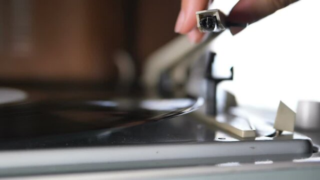 Close-up of woman hand placing needle on a vinyl record player, slow motion