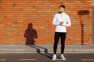 Handsome athlete young man against a brick wall looking at camera in sunset light. Sports man in sportwear after workout .