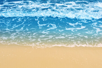 Fototapeta na wymiar Soft wave of blue ocean on sandy beach. Background. Empty beach with sea foam washing up from sea.