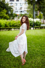 Fototapeta na wymiar Young woman in dress posing in summer park. Caucasian girl enjoys a bright summer lifestyle. Concept of summer,outdoors and leisure activity