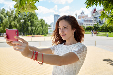 Selfie time.Joyful attractive young woman making selfie by her smart phone in the summer park.Caucasian girl enjoys a bright summer lifestyle