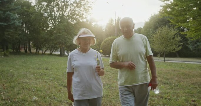 Backlit elderly couple walking in a park chatting and carrying a bottle of water in a healthy active lifestyle concept in retirement