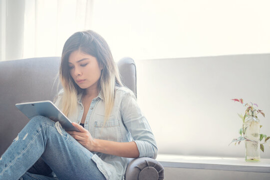 Girl working at home with tablet on armchair.