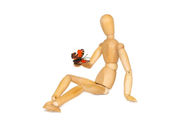Wooden dummy and butterfly on white background. The figure of a wooden mannequin holds a butterfly in his hands. The concept of spring, freedom and life. Concept of protecting ecology and nature.