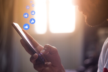 man holding smart phone in house with like icons hovering over the screen social media concept