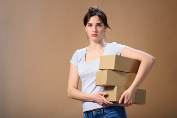 European girl holds several boxes in her hands with her side and looks at the camera directly on a beige wall