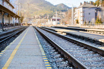 Fototapeta premium Empty train station in small city on sunny day, shallow depth of field photo, focus on concrete platform and steel rail foreground