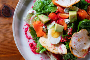 Vegetable salad with egg, tomato, pomegranate and avocado. A healthy dish on a white plate in a restaurant close-up.