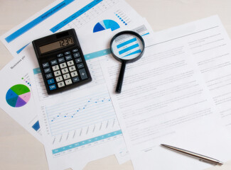 Magnifying glass with a calculator with pen on the background of business charts.