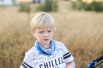 Fototapeta premium Young blonde boy sitting on bike on dry country lane