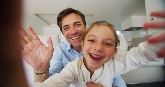 Authentic shot of happy smiling father and daughter are making a selfie or video call to a mother or relatives on a sofa in a living room.