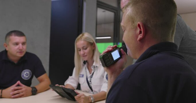 Security guard monitoring modern CCTV cameras in a surveillance room. Group of security guards sitting and having conversation.