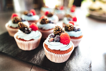 Closeup of delicious miniature cakes. Raspberry, blueberry and blackberry decorated cupcakes. Celebration, party, birthday or wedding concept.