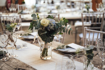 Festive table arrangement. White and blue flower bouquet in transparent glass vase. Celebration, wedding, birthday concept.
