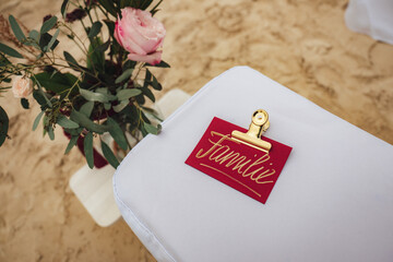Golden written text familie on red paper with golden clip laying on white cloth. Pink flower and...
