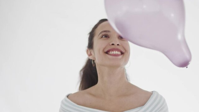 Attractive young dark-haired woman with ponytail flinging purple baloon around and looking at it with broad smile and exitement. 360 degree tracking arc shot in 4K.