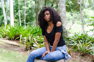 a young black woman between 20 and 30 years old sitting reading a book alone, in a park