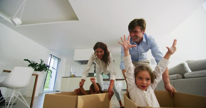 Authentic shot of carefree happy smiling parents and daughters are having fun to racing with empty box just moved into a new house.