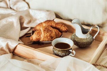 Romantic morning atmosphere, breakfast in bed. French croissants, cup of coffee and milkman on a wooden tray on a silk bed. Lifestyle 
