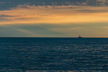 Fototapeta na wymiar Sunset over sea water, after the thunderstorm. Full of clouds and vibrant colors over horizon. And one thugboat waiting for oil tanker. 
