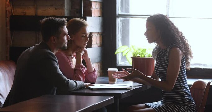 Female african manager broker saleswoman consult family customers make mortgage insurance loan offer, advisor agent insurer explain couple clients deal benefit convince buy service at meeting in cafe