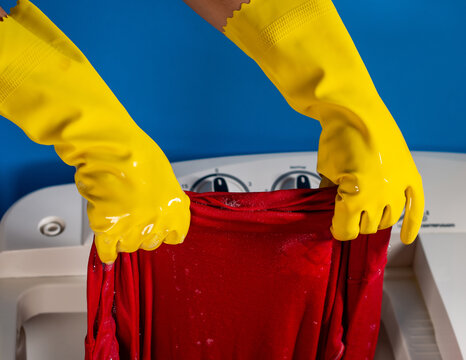 girl hands with yellow cleaning gloves taking out a shirt from washing machine and blue background