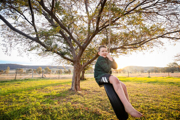 Young boy playing on backyard tire swing during vibrant sunset