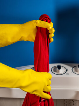hands squeezing a red shirt from a white washing machine and a blue background