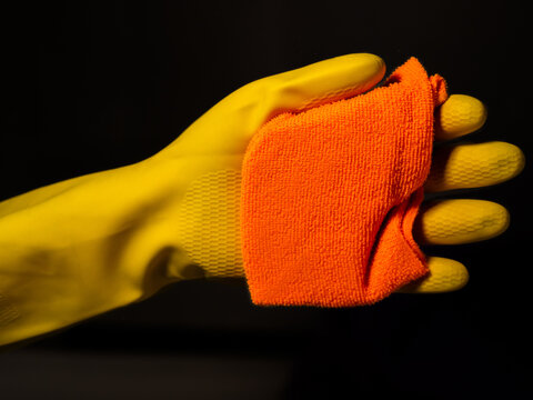 yellow gloved hands with orange rag cleaning a glass and dark background