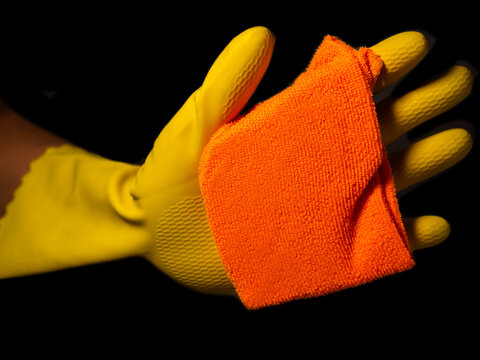 hands in yellow cleaning glove with an orange cloth wiping a glass and a black background