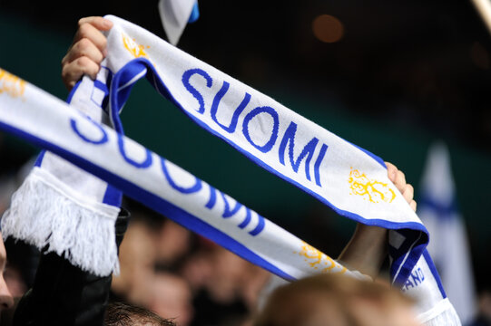Sports spectators waiving two fabric fan scarfs stating Suomi - Finland.