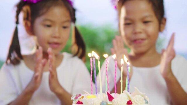 Close up of candle on  birthday cake with asian little girls are singing and blowing candle at home together. Kids having fun on birthday party. Slow motion