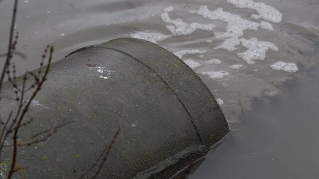 Dirty waste water flowing out of concrete drainage pipe into the city pond.
