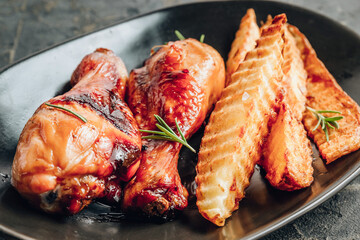 Chicken drumsticks with french fries on black plate on rustic black background.