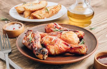 Chicken drumsticks on brown plate and french fries on white plate on wooden table.