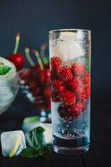 Cold lemonade with raspberries, lemon, ice and cherries on black background