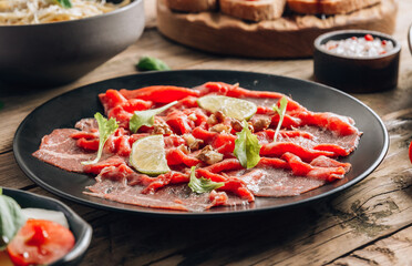 Black plate with carpaccio of beef with baby arugul and lime on rustic wooden background.