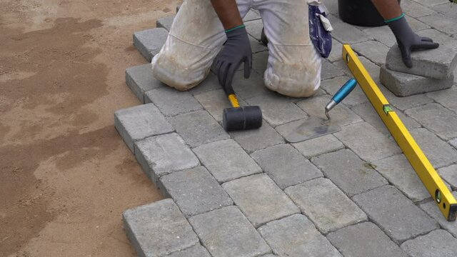 A craftsman lays concrete paving stone blocks on sand. Paving stone work.