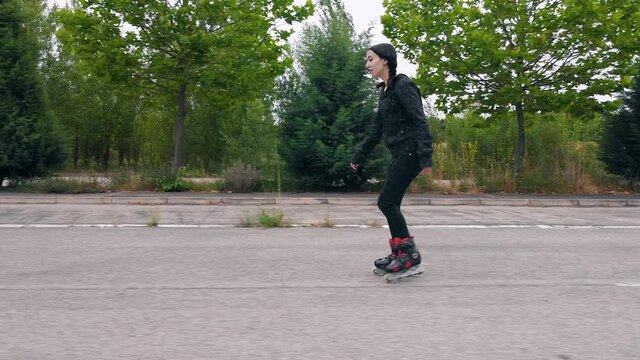Follow shot, lateral view of young woman practicing roller skating on road. High quality 4k footage