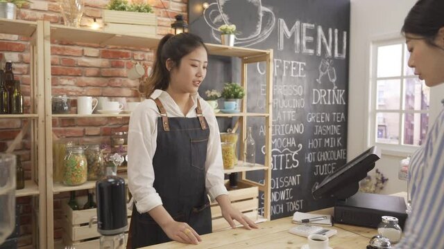 Young female customer taking coffee from barista in counter of coffee shop. asian businesswoman employee taking hot cup with tea doing payment giving credit card to waitress in modern cafe bar.