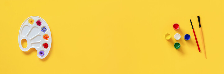 Colorful flowers on artistic palette, brush, gouache on yellow background, copy space. Creative concept summer colors or International Flower Day. Top view Flat lay Banner