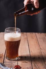 bartender serving beer with a glass bottle on a rustic wooden table and dark environment.
